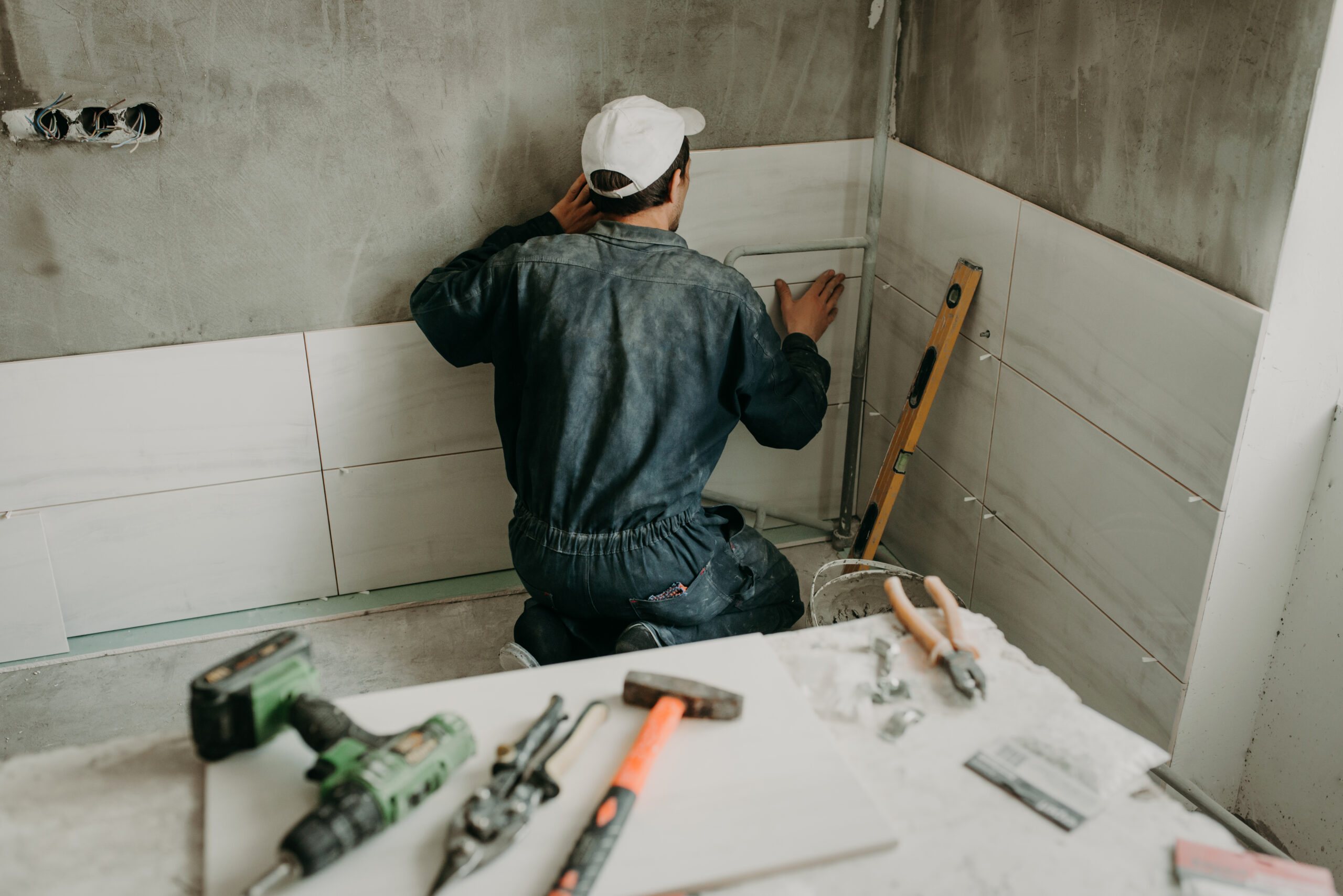 worker repairman puts large ceramic tiles on the walls in the room