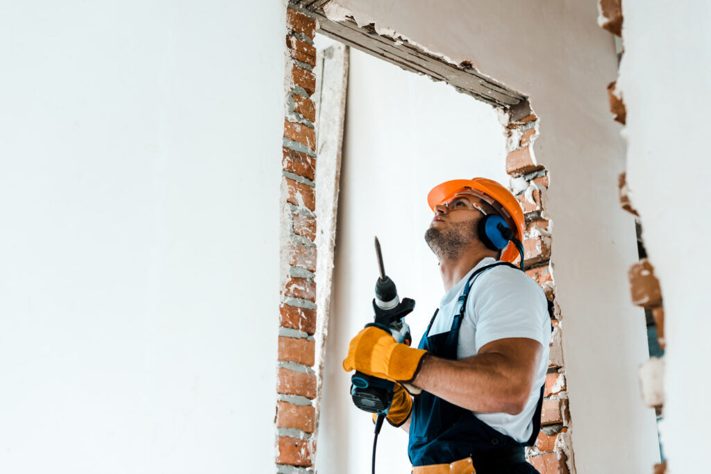 handsome workman holding hammer drill and looking at wall